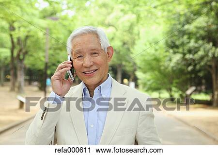 Stock Image - Senior adult Japanese man with smartphone in a park. Fotosearch