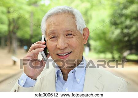 Stock Image - Senior adult Japanese man with smartphone in a park. Fotosearch