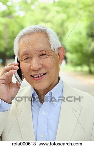 Stock Image - Senior adult Japanese man with smartphone in a park. Fotosearch