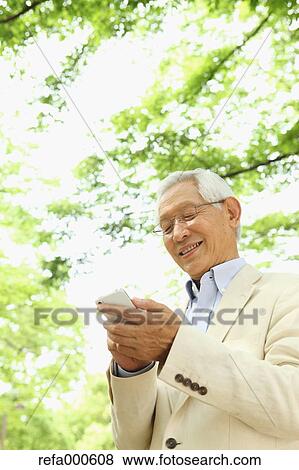Stock Photo - Senior adult Japanese man with smartphone in a park. Fotosearch