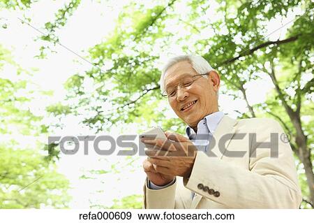 Senior adult Japanese man with smartphone in a park View Large Photo Image Stock Photo - Senior adult Japanese man with smartphone in a park. Fotosearch