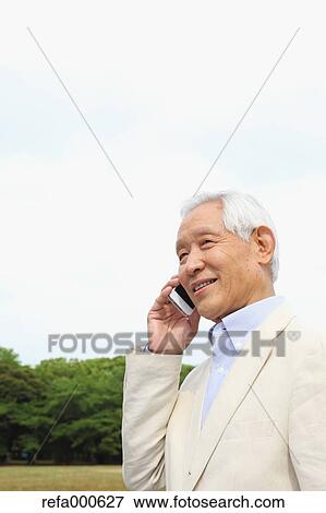 Stock Photo - Senior adult Japanese man with smartphone in a park. Fotosearch