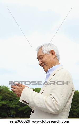 Stock Photo - Senior adult Japanese man with smartphone in a park. Fotosearch