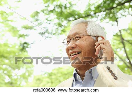 Stock Photograph - Senior adult Japanese man with smartphone in a park. Fotosearch