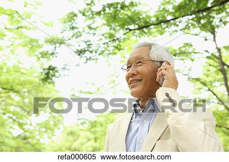 Stock Photography - Senior adult Japanese man with smartphone in a park. Fotosearch