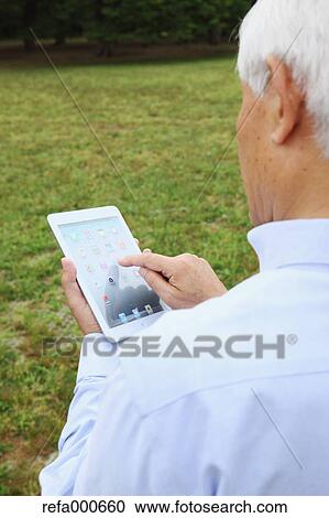 Stock Image - Senior adult Japanese man with tablet in a park. Fotosearch