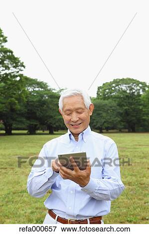 Senior adult Japanese man with tablet in a park View Large Photo Image Stock Photo - Senior adult Japanese man with tablet in a park. Fotosearch