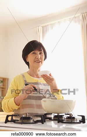 Stock Image - Senior adult Japanese woman cooking. Fotosearch