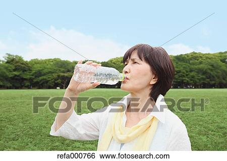 Stock Photograph - Senior adult Japanese woman drinking water in a park. Fotosearch