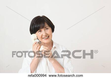 Picture - Senior adult Japanese woman with phone against white wall. Fotosearch