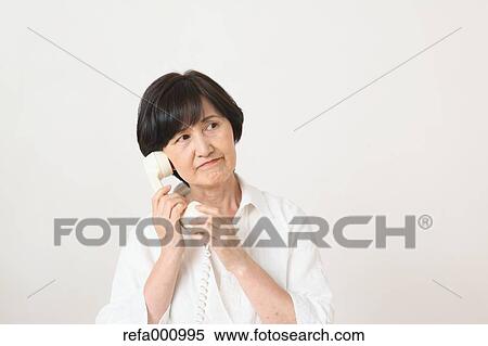 Stock Photography - Senior adult Japanese woman with phone against white wall. Fotosearch