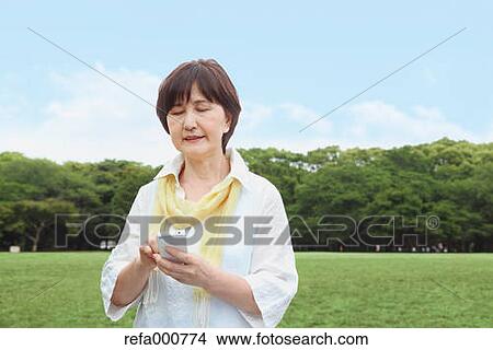 Senior adult Japanese woman with smartphone in a park View Large Photo Image Picture - Senior adult Japanese woman with smartphone in a park. Fotosearch