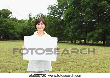 Stock Image - Senior adult Japanese woman with whiteboard in a park. Fotosearch