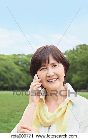 Stock Image - Senior adult Japanese woman with smartphone in a park. Fotosearch