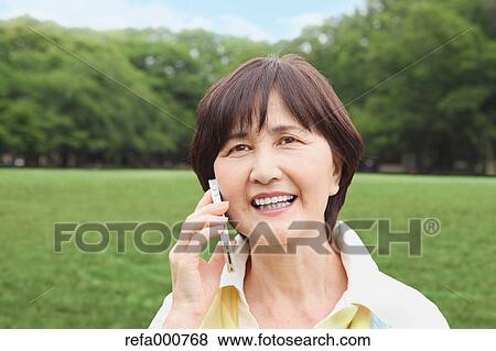 Stock Photo - Senior adult Japanese woman with smartphone in a park. Fotosearch