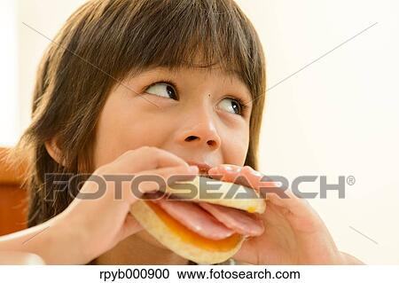 Stock Image - Young boy eating in the kitchen. Fotosearch