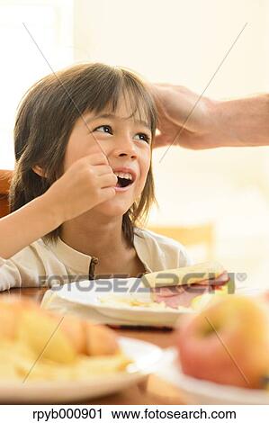 Stock Image - Young boy eating in the kitchen. Fotosearch