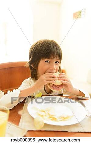 Stock Photograph - Young boy eating in the kitchen. Fotosearch