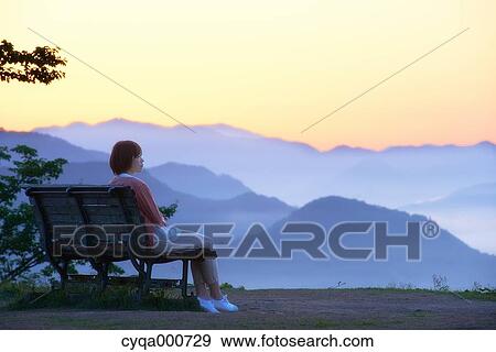 Stock Photo - Young Japanese woman sitting on a bench in the countryside. Fotosearch