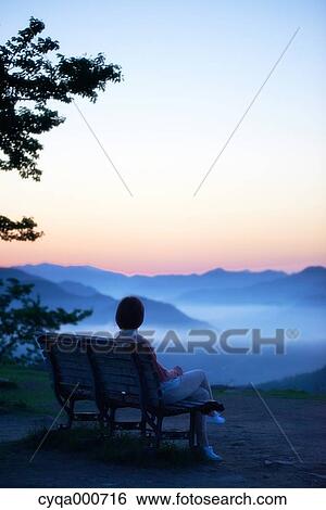 Stock Photograph - Young Japanese woman sitting on a bench in the countryside. Fotosearch