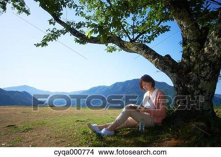 Picture - Young Japanese woman sitting with book in the countryside. Fotosearch