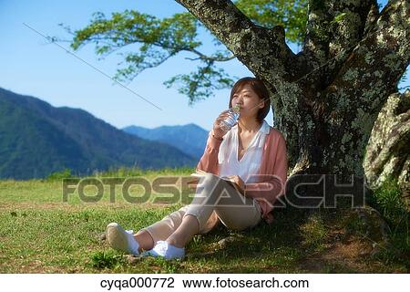 Young Japanese woman sitting with book in the countryside drinking water View Large Photo Image Stock Image - Young Japanese woman sitting with book in the countryside drinking water. Fotosearch