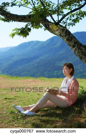 Young Japanese woman sitting with book in the countryside View Large Photo Image Stock Photo - Young Japanese woman sitting with book in the countryside. Fotosearch