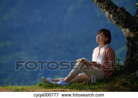Stock Photo - Young Japanese woman sitting with book in the countryside. Fotosearch