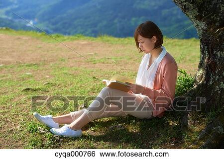 Stock Photograph - Young Japanese woman sitting with book in the countryside. Fotosearch