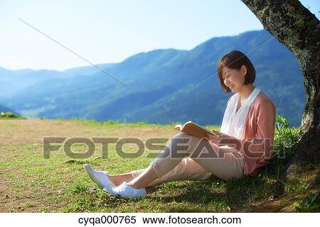 Stock Photography - Young Japanese woman sitting with book in the countryside. Fotosearch