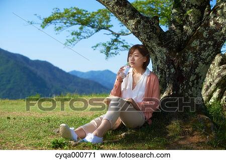 Young Japanese woman sitting with water and book in the countryside View Large Photo Image Stock Image - Young Japanese woman sitting with water and book in the countryside. Fotosearch