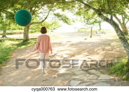 Stock Image - Young Japanese woman with green balloon in the countryside. Fotosearch