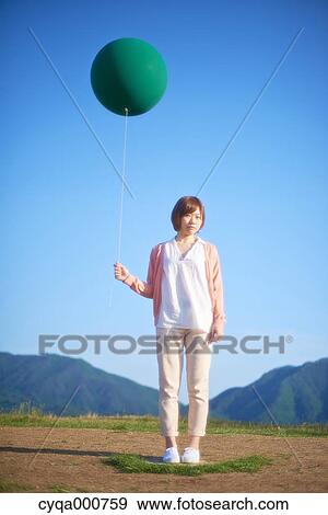 Stock Photo - Young Japanese woman with green balloon in the countryside. Fotosearch