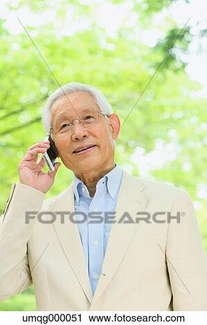 Stock Image - Senior adult Japanese man with smartphone in a park. Fotosearch