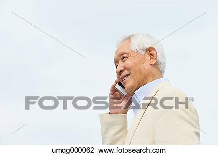 Stock Image - Senior adult Japanese man with smartphone in a park. Fotosearch