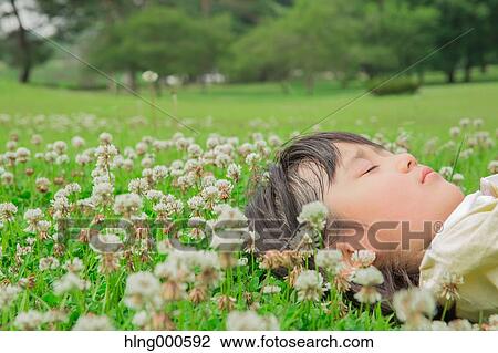 Stock Image - Japanese kid laying on grass in a park. Fotosearch