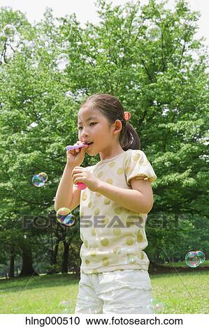 Stock Image - Japanese kid playing with soap bubbles in a park. Fotosearch