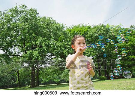 Stock Photo - Japanese kid playing with soap bubbles in a park. Fotosearch