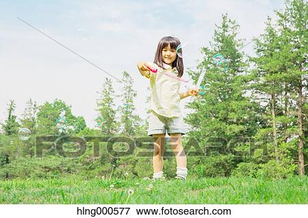 Stock Photo - Japanese kid playing with soap bubbles in a park. Fotosearch