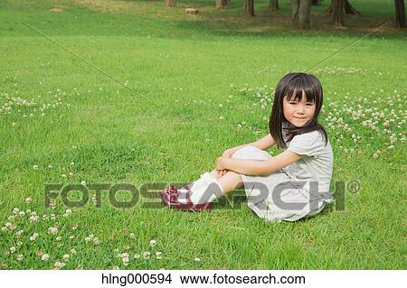 Picture - Japanese kid sitting on grass in a park. Fotosearch