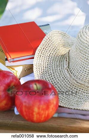 Stock Photo - Apples and straw hat on deck chair in a city park. Fotosearch