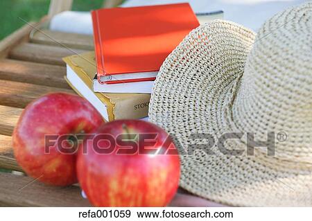 Stock Photo - Apples and straw hat on deck chair in a city park. Fotosearch