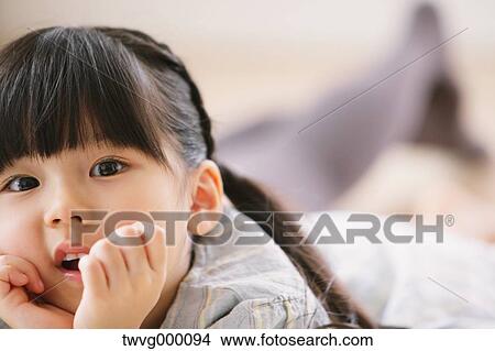Picture - Close up of elementary age girl lying on the floor and looking at camera. Fotosearch