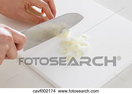 Picture - Close up of woman's hands slicing onions with a kitchen knife. Fotosearch