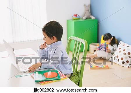 Elementary age boy doing his homework at his desk with his sister reading on the floor in the background View Large Photo Image Stock Image - Elementary age boy doing his homework at his desk with his sister reading on the floor in the background. Fotosearch