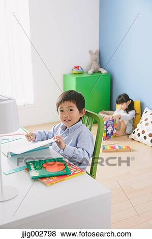 Elementary age boy doing his homework at his desk with his sister reading on the floor in the background View Large Photo Image Stock Photo - Elementary age boy doing his homework at his desk with his sister reading on the floor in the background. Fotosearch