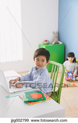 Elementary age boy doing his homework at his desk with his sister reading on the floor in the background View Large Photo Image Stock Photo - Elementary age boy doing his homework at his desk with his sister reading on the floor in the background. Fotosearch