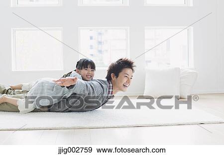 Stock Photo - Elementary age girl laying on his fathers back and smiling. Fotosearch