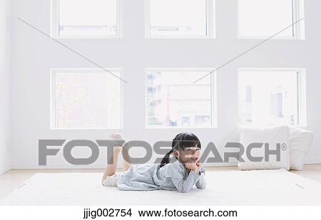 Picture - Elementary age girl laying on the floor by the window. Fotosearch