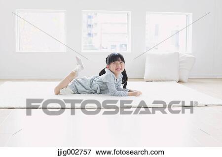 Stock Photo - Elementary age girl laying on the floor by the window and smiling. Fotosearch